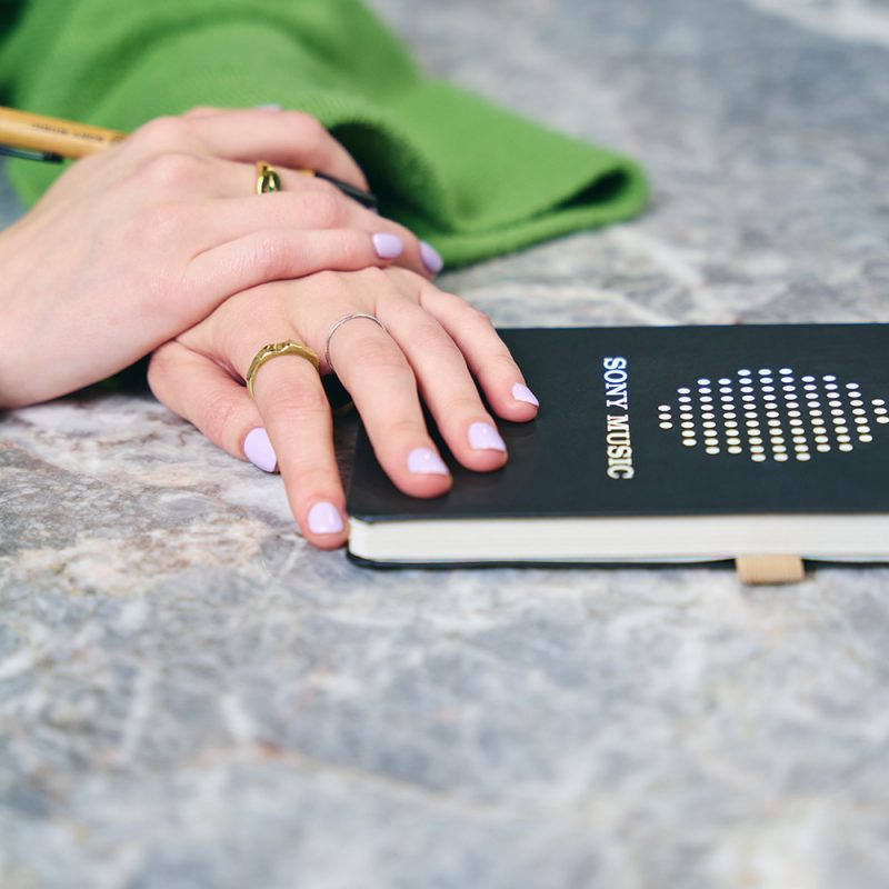 A pair of hands resting on top of a Sony Music notebook.