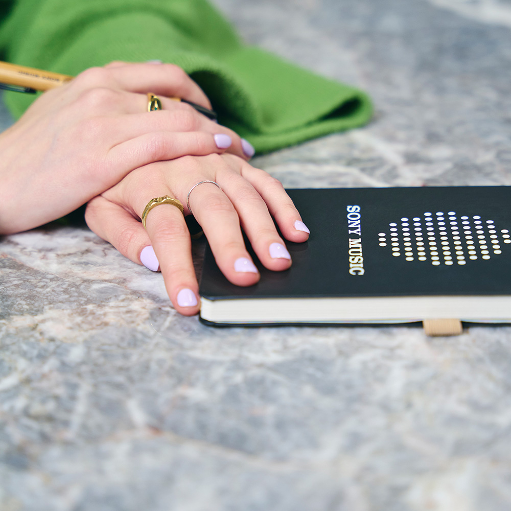 A pair of hands resting on top of a Sony Music notebook.